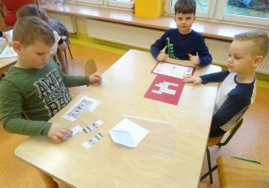 Dwoje dzieci rozwiązuje krzyżówkę. Jeden chłopiec składa obrazek z części.